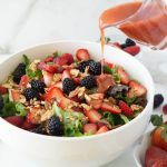 Large bowl of berry salad with strawberry vinaigrette being drizzled on top
