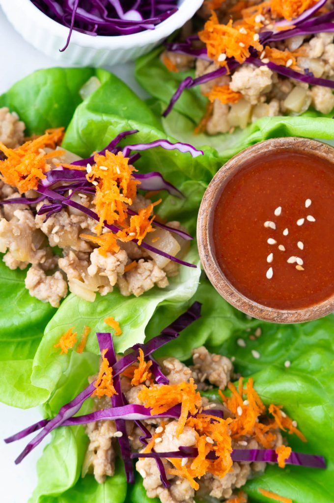 Three sesame chicken lettuce wraps topped with shredded carrots and red cabbage
