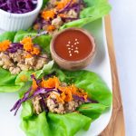 A row of sesame chicken lettuce wraps topped with shredded carrots and red cabbage