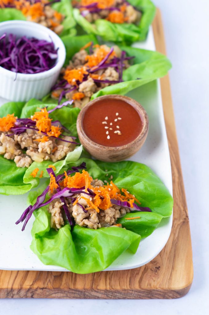 A row of sesame chicken lettuce wraps topped with shredded carrots and red cabbage