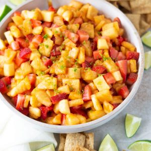 A bowl of fruit salsa with lime zest surrounded by lime wedges and cinnamon chips