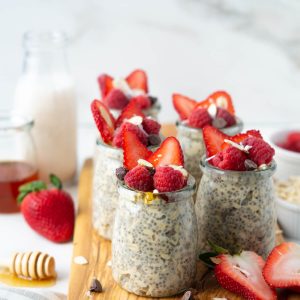 Jars of protein overnight oats topped with berries, chocolate chips, and a drizzle of honey sitting on a wooden board.