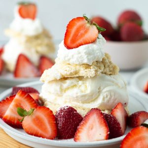 Vanilla ice cream sandwiched between two biscuit pieces, topped with whipped cream and strawberries