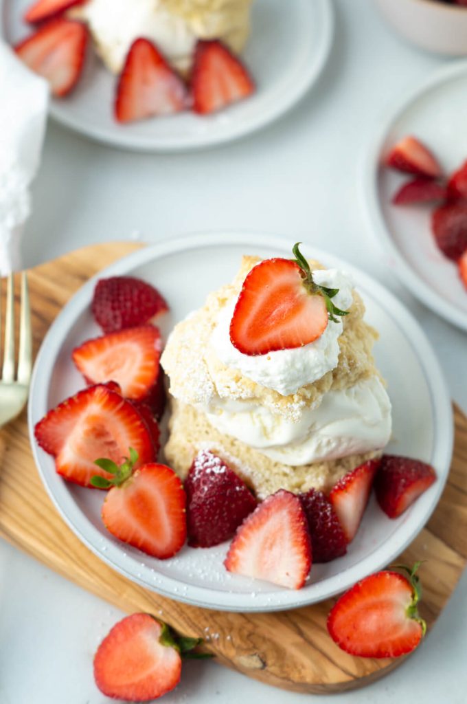 Vanilla ice cream sandwiched between two biscuit pieces, topped with whipped cream and strawberries to make strawberry shortcake