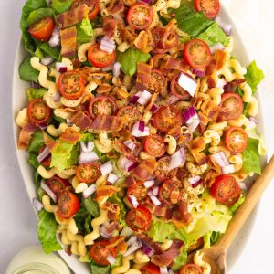 An overhead view of a large platter of BLT Banza Pasta Salad with a jar of jalapeño ranch dressing.