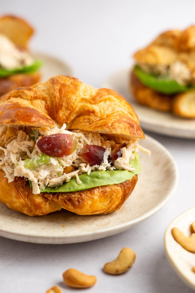 Shot of a croissant filled with Chicken salad sandwich and lettuce with cashews to the side.