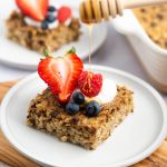 Honey being drizzled on top of a piece cookie dough baked oats that is topped with Greek yogurt and fresh berries