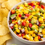 A large bowl of corn mango salsa served with tortilla chips.