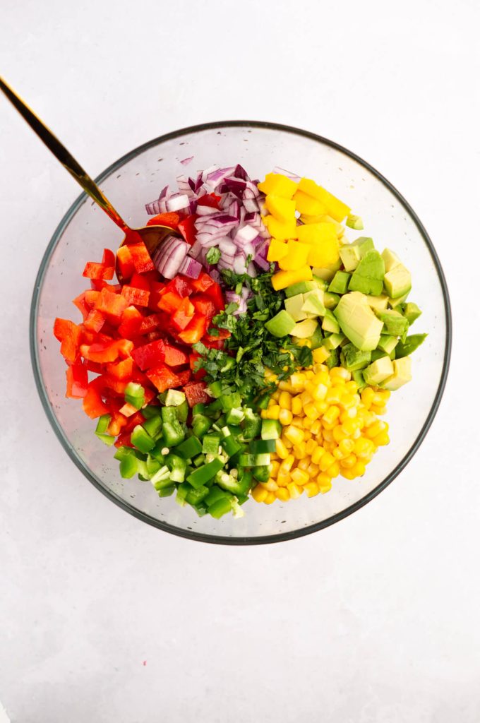 A large bowl with the unmixed ingredients for corn mango salsa.