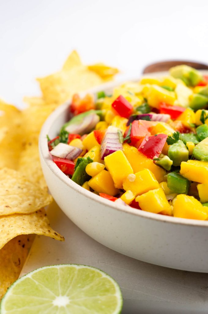 A large bowl of corn mango salsa served with tortilla chips.