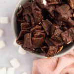 A bowl of S'mores Mix with mini marshmallows scattered around it.