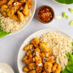 Two bowls of air fryer orange chicken with brown rice and a lettuce garnish.