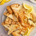 Photo of air fryer pita chips with hummus and lemon slices and a gold spoon.