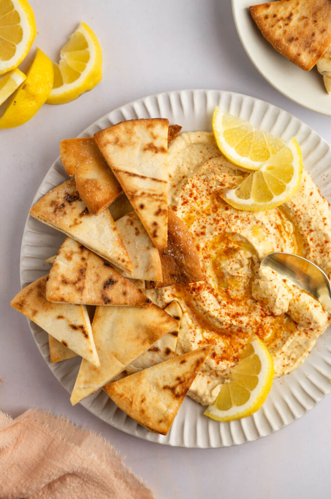 Photo of air fryer pita chips with hummus and lemon slices and a gold spoon.