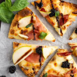 Photo of blackberry pizza cut with basil and blackberries.