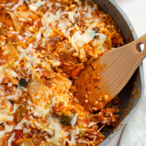 Lasagna skillet with cottage cheese and a wooden spoon dishing up.