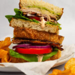 Roasted turkey bacon avocado BLT cut in half and stacked with chips on the side.