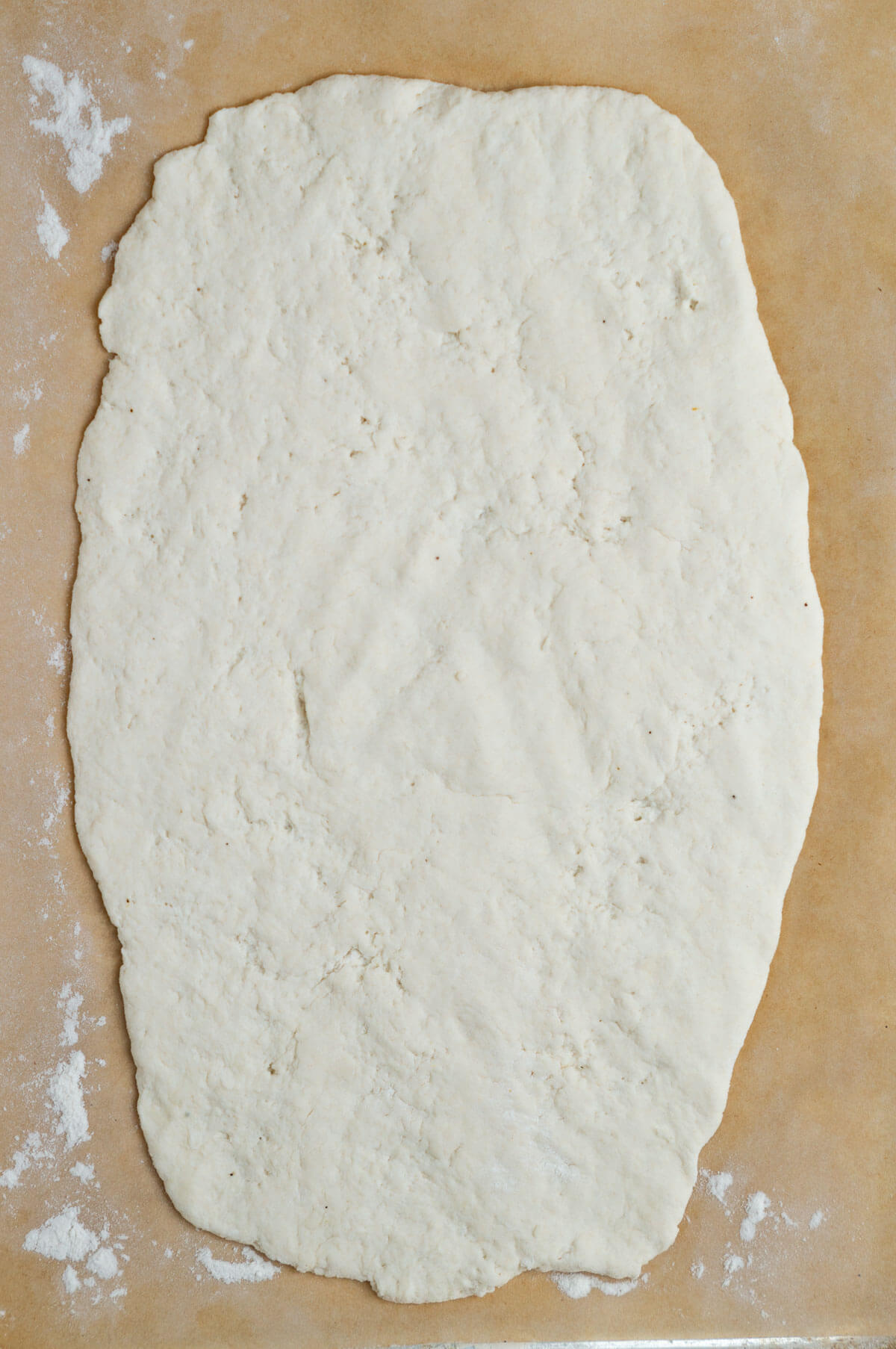 A piece of parchment paper with pizza dough on top that is rolled out into the shape of a rectangle.