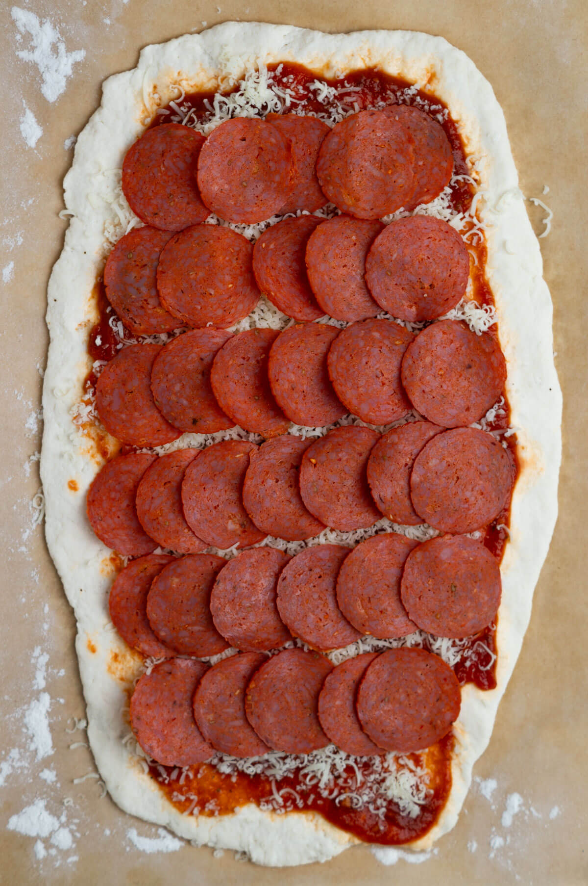 A rectangle of pizza dough with marinara sauce, shredded mozzarella cheese, and turkey pepperoni layered on top.