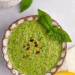Bowl of basil cashew pesto with basil leaves, lemon, and red pepper flakes.