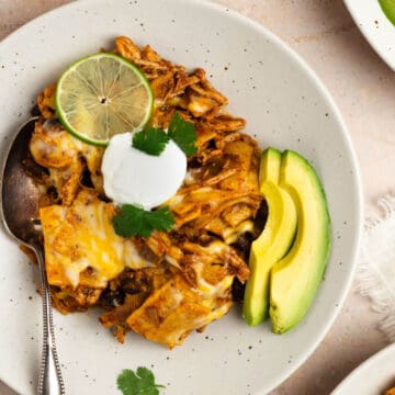 An overhead shot of a bowl with crockpot chicken enchiladas topped with sour cream, lime, avocado, and cilantro.