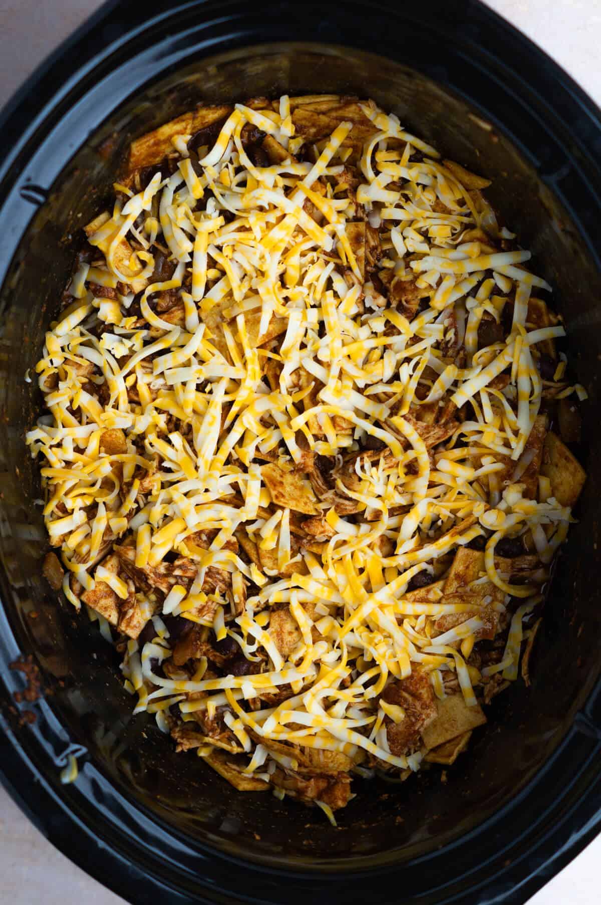 Overhead shot of the slow cooker enchiladas topped with shredded cheese.