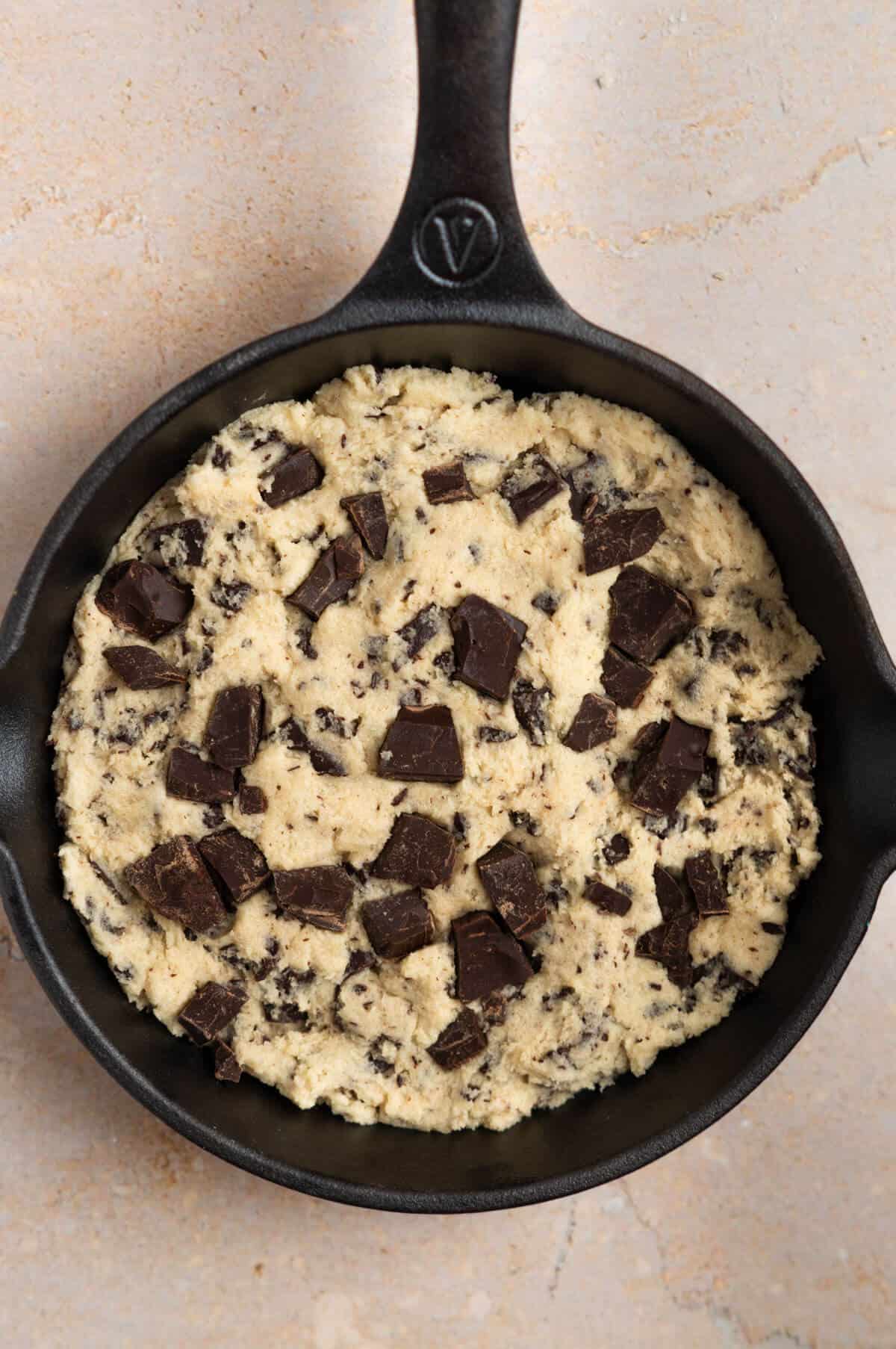 An overhead shot of a mini skillet with cookie dough pressed inside and chocolate chunks sprinkled on top.
