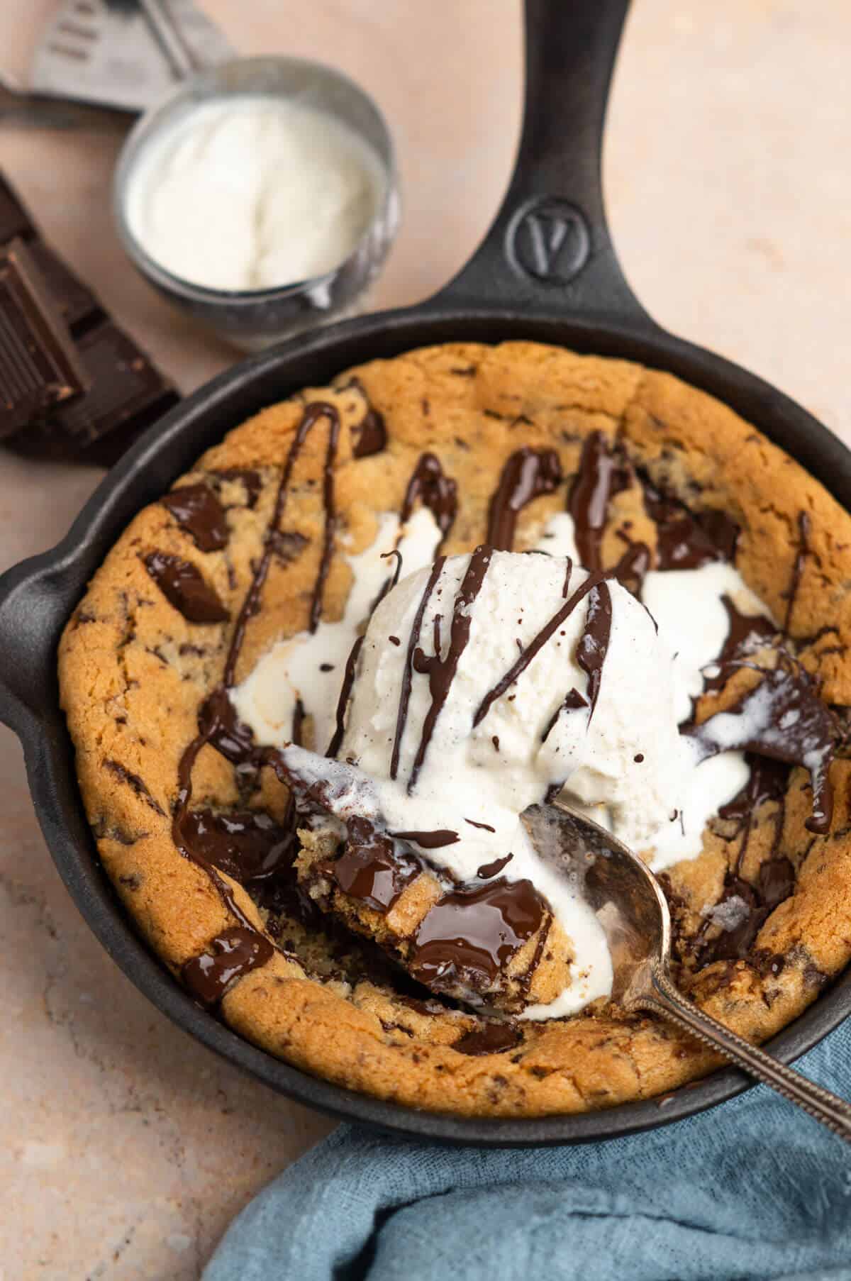 A baked chocolate chip cookie mini skillet with vanilla ice cream and a drizzle of melted chocolate.