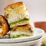 Two stacked pesto chicken sliders on a plate with a third slider leaning against the stack.