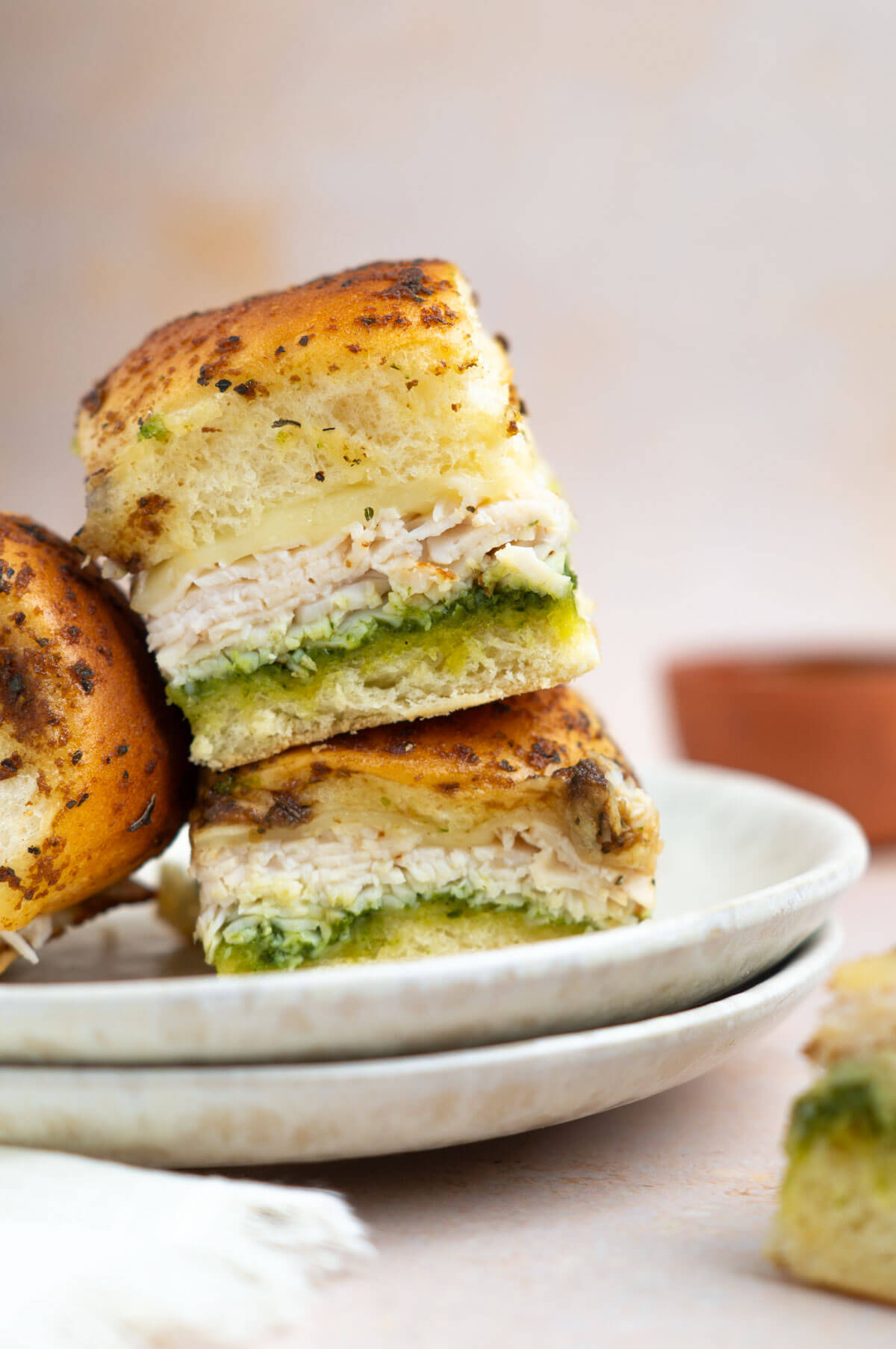 Two stacked pesto chicken sliders on a plate with a third slider leaning against the stack.