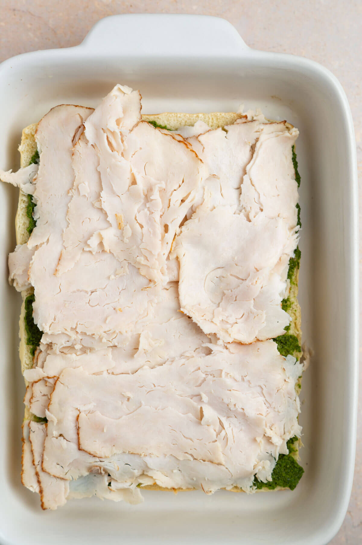 An overhead shot of the bottom half of the Hawaiian rolls with pesto and sliced chicken breast spread across it.