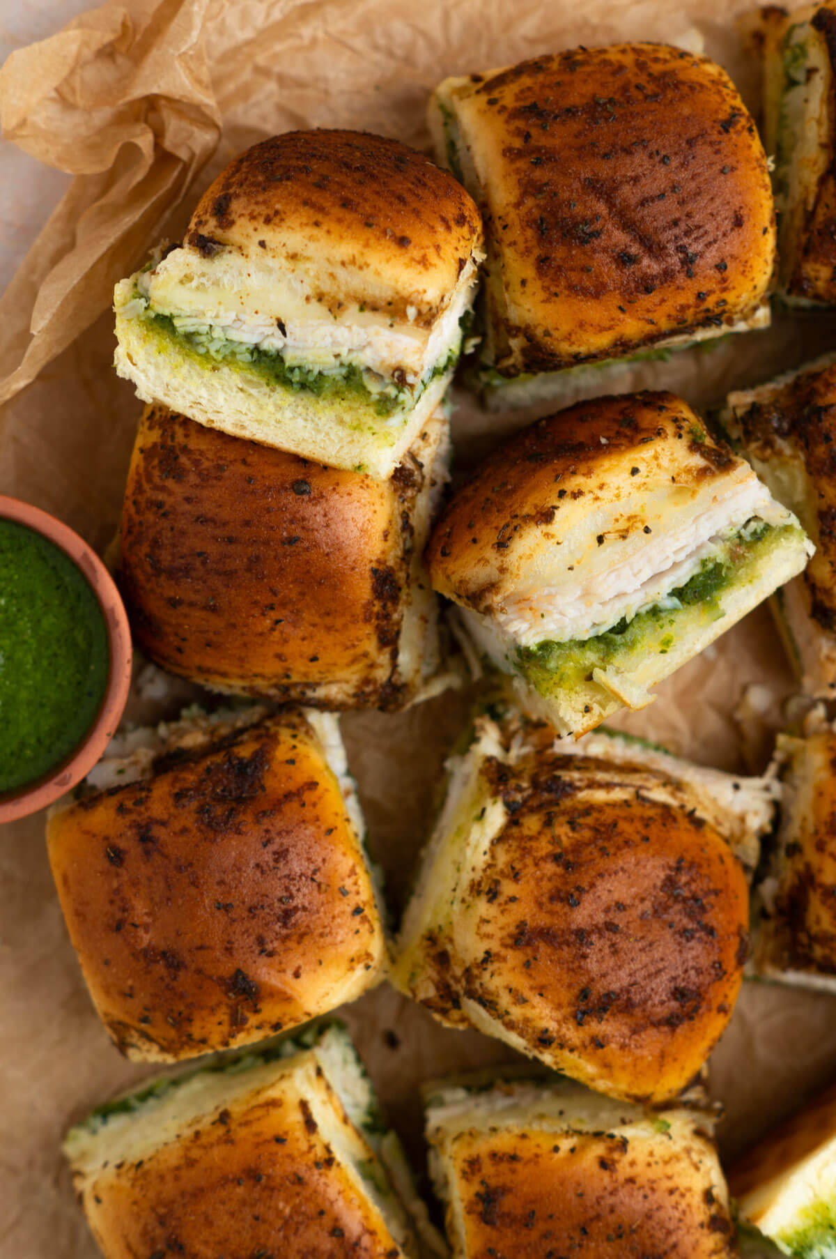 Eight pesto chicken sliders lined up with two sliders on their sides to show the contents of the sandwiches.