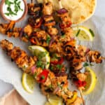 An overhead shot of five Tandoori Chicken Kebabs with pita bread, lemon slices, and a side dip of Greek yogurt.