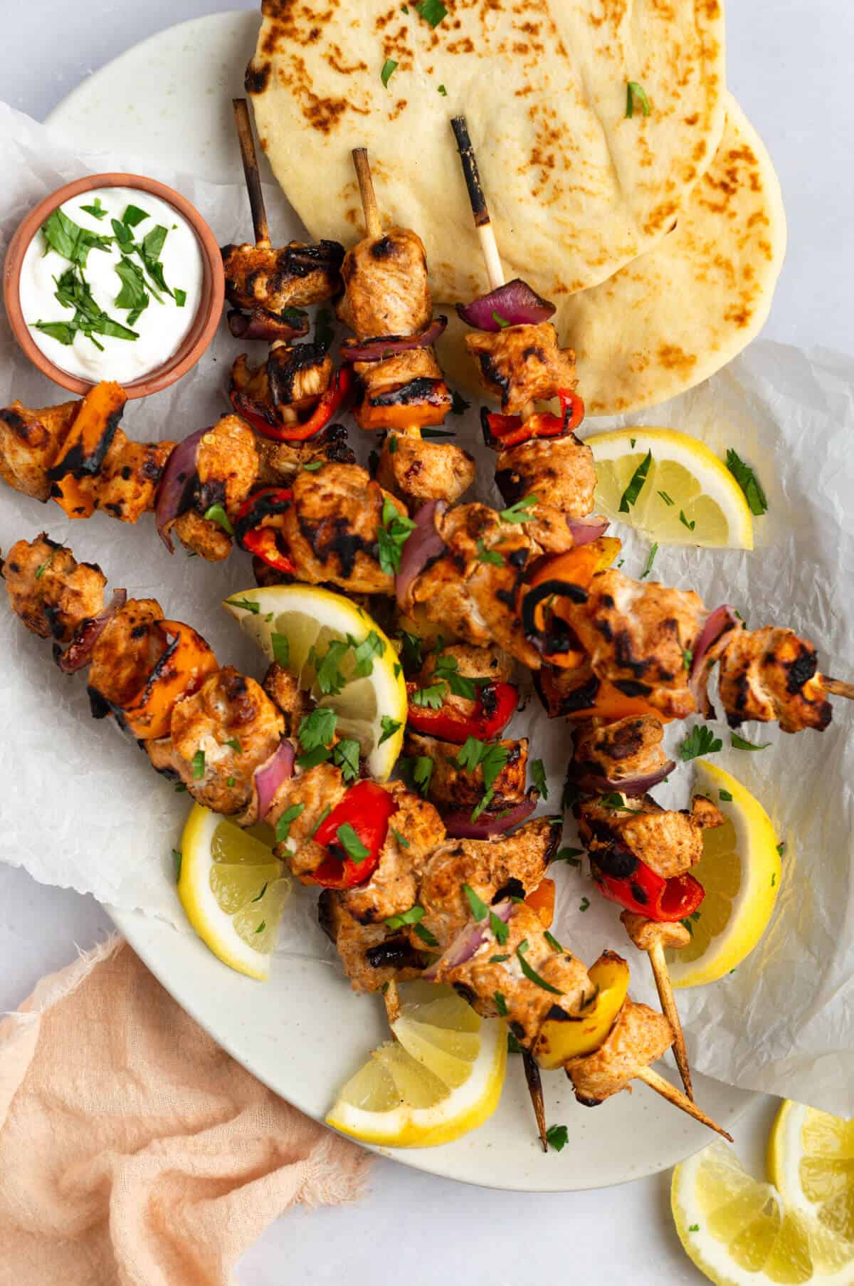 An overhead shot of five Tandoori Chicken Kebabs with pita bread, lemon slices, and a side dip of Greek yogurt.