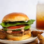 Turkey smash burger with lettuce, tomato, bacon, BBQ ranch, and fries and soda in the background.