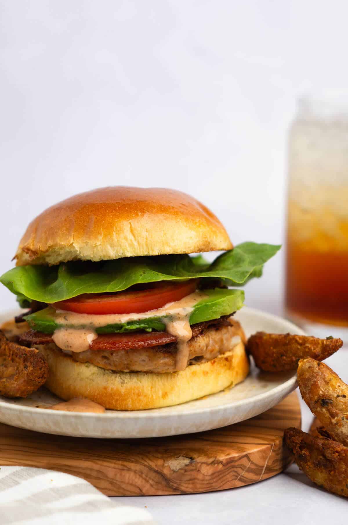 Turkey smash burger with lettuce, tomato, bacon, BBQ ranch, and fries and soda in the background.