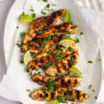 An overhead shot of a platter of grilled cilantro ginger chicken garnished with chopped cilantro and lime wedges.