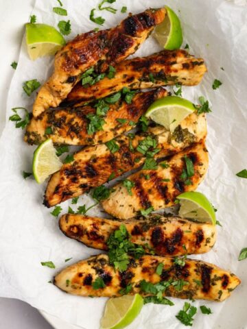 An overhead shot of a platter of grilled cilantro ginger chicken garnished with chopped cilantro and lime wedges.