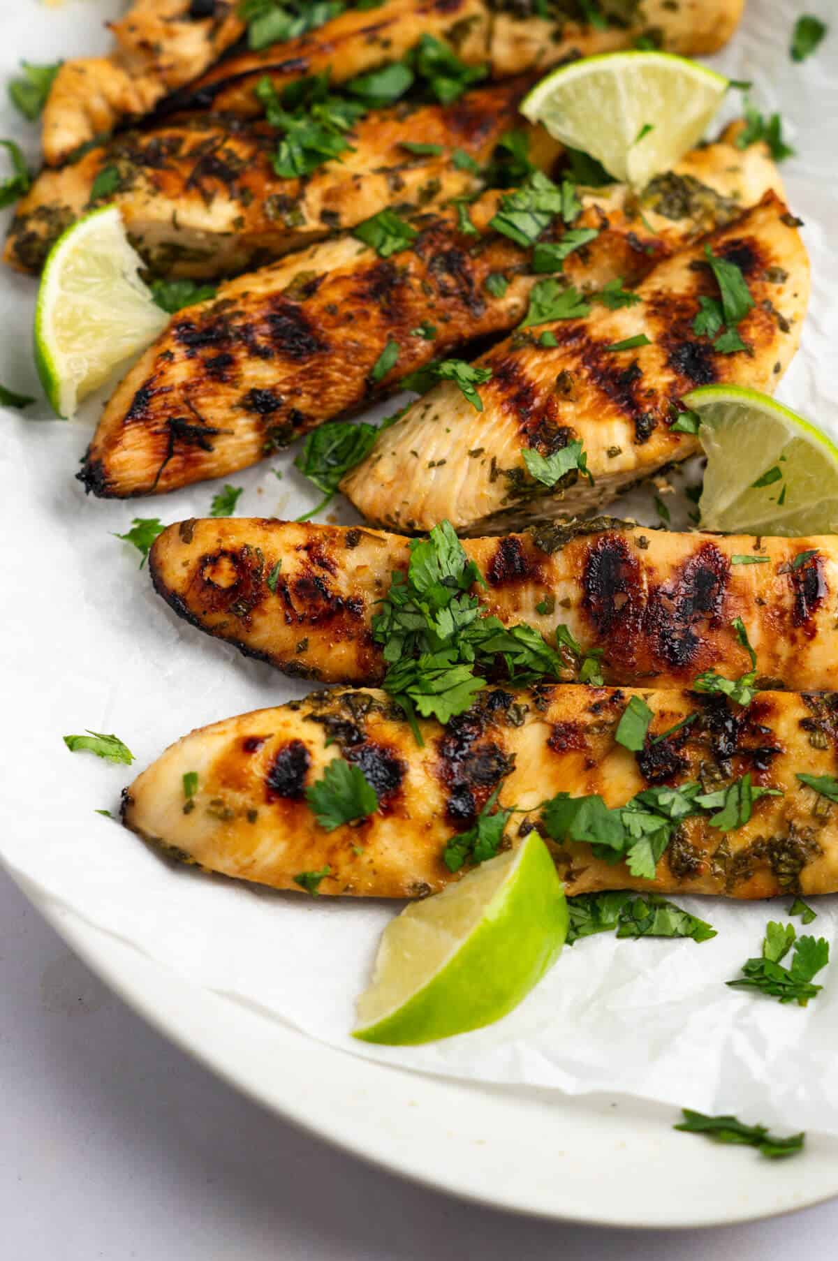 And up close shot of a platter of grilled ginger cilantro chicken with chopped cilantro and lime wedge garnishes.