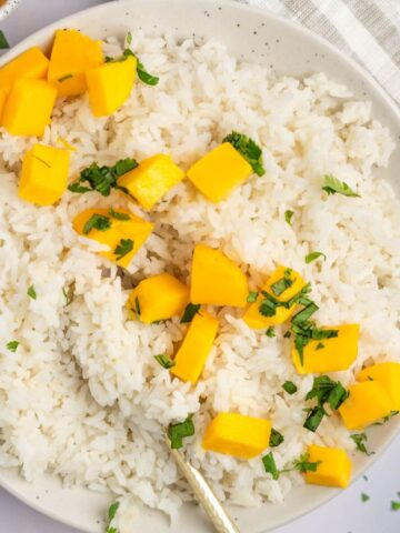 An overhead shot of a large bowl of coconut jasmine rice with diced mango and chopped cilantro.