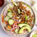 An overhead shot of a bowl with white rice, Korean ground turkey, pickled veggies, avocado slices, and sliced shallots.