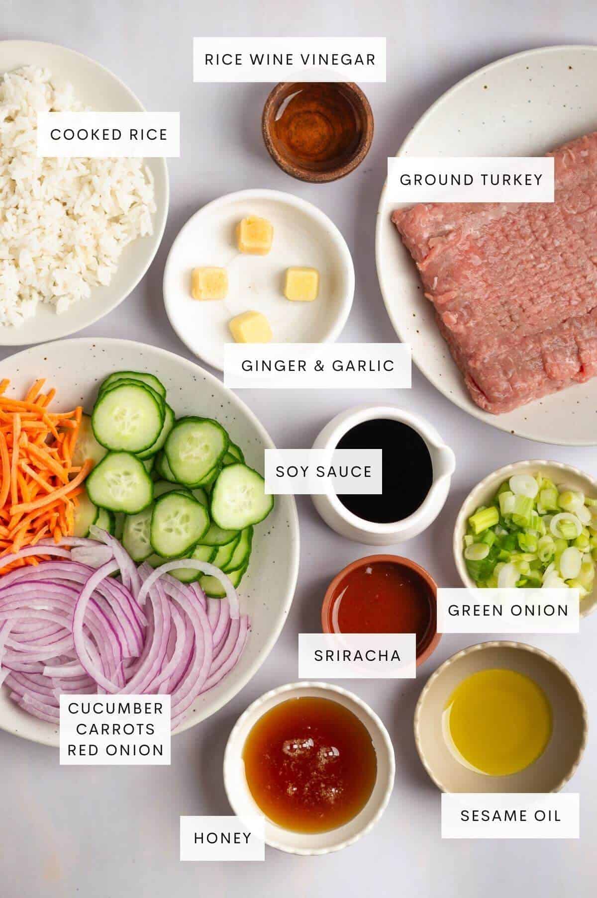 Ingredients needed for Korean inspired ground turkey bowls: rice, ground turkey, rice wine vinegar, ginger, garlic, soy sauce, green onion, Sriracha, sesame oil, honey, and sliced cucumbers, carrots, and red onion.
