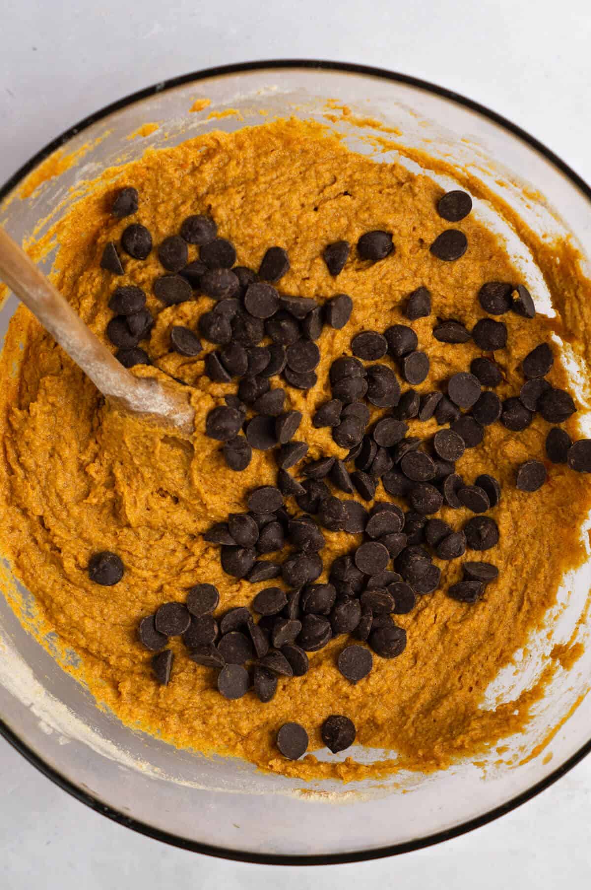 A mixing bowl with batter for pumpkin protein muffins with chocolate chips added in.