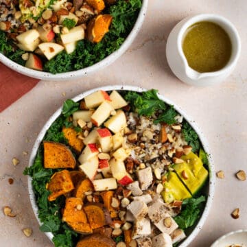 An overhead shot of two bowls filled with the harvest bowl salad with a small container of dressing to the side.