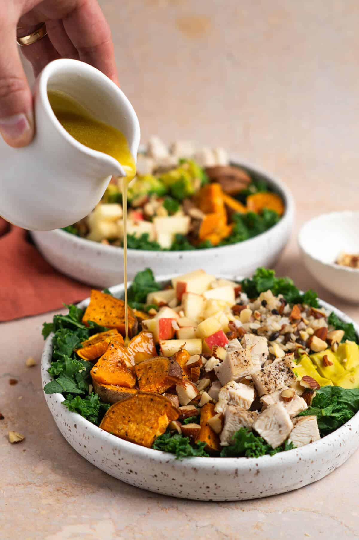 An assembled harvest bowl and balsamic dressing being drizzled over the top of the salad.
