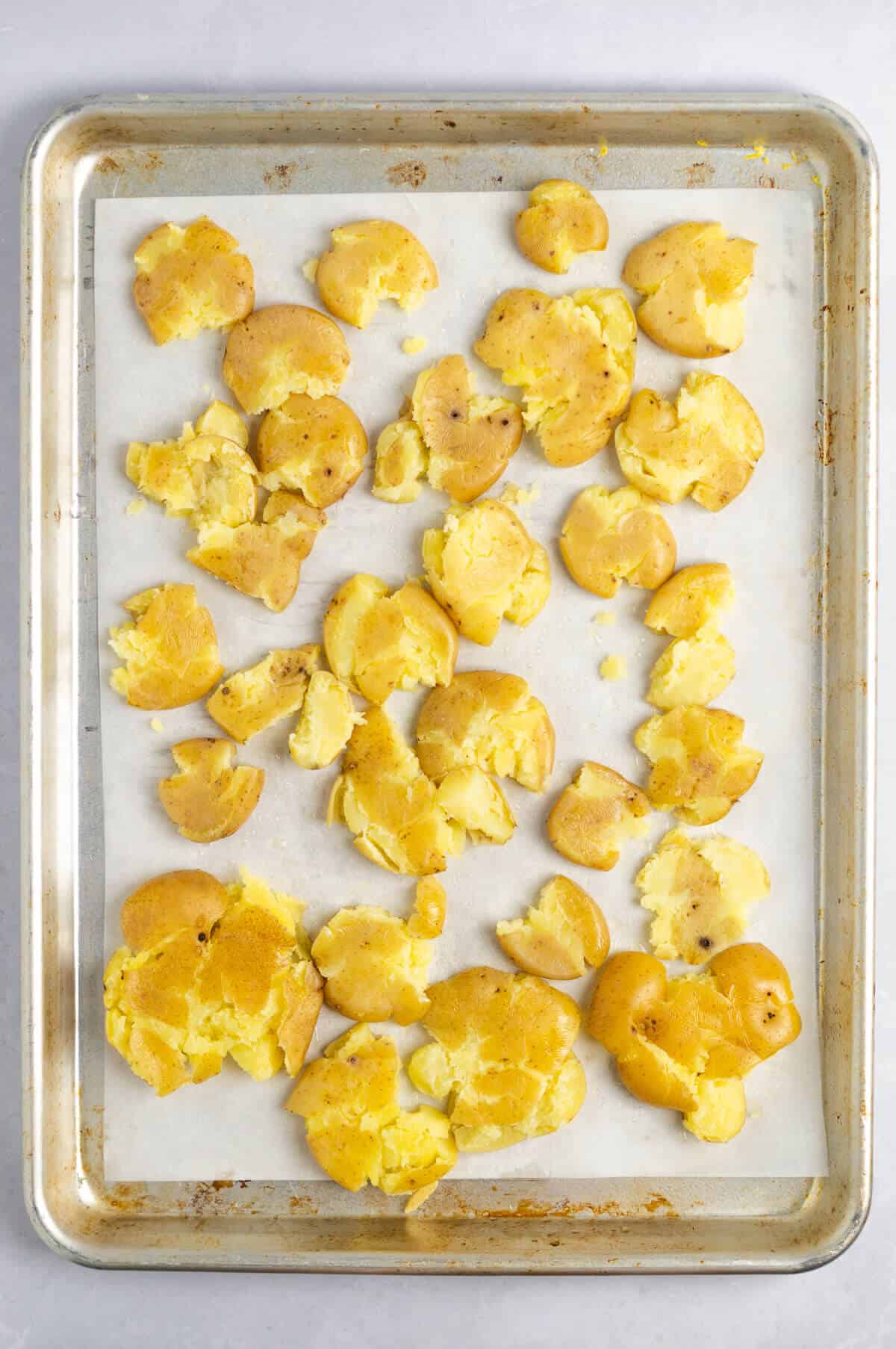 A parchment-lined baking sheet with smashed baby potatoes.
