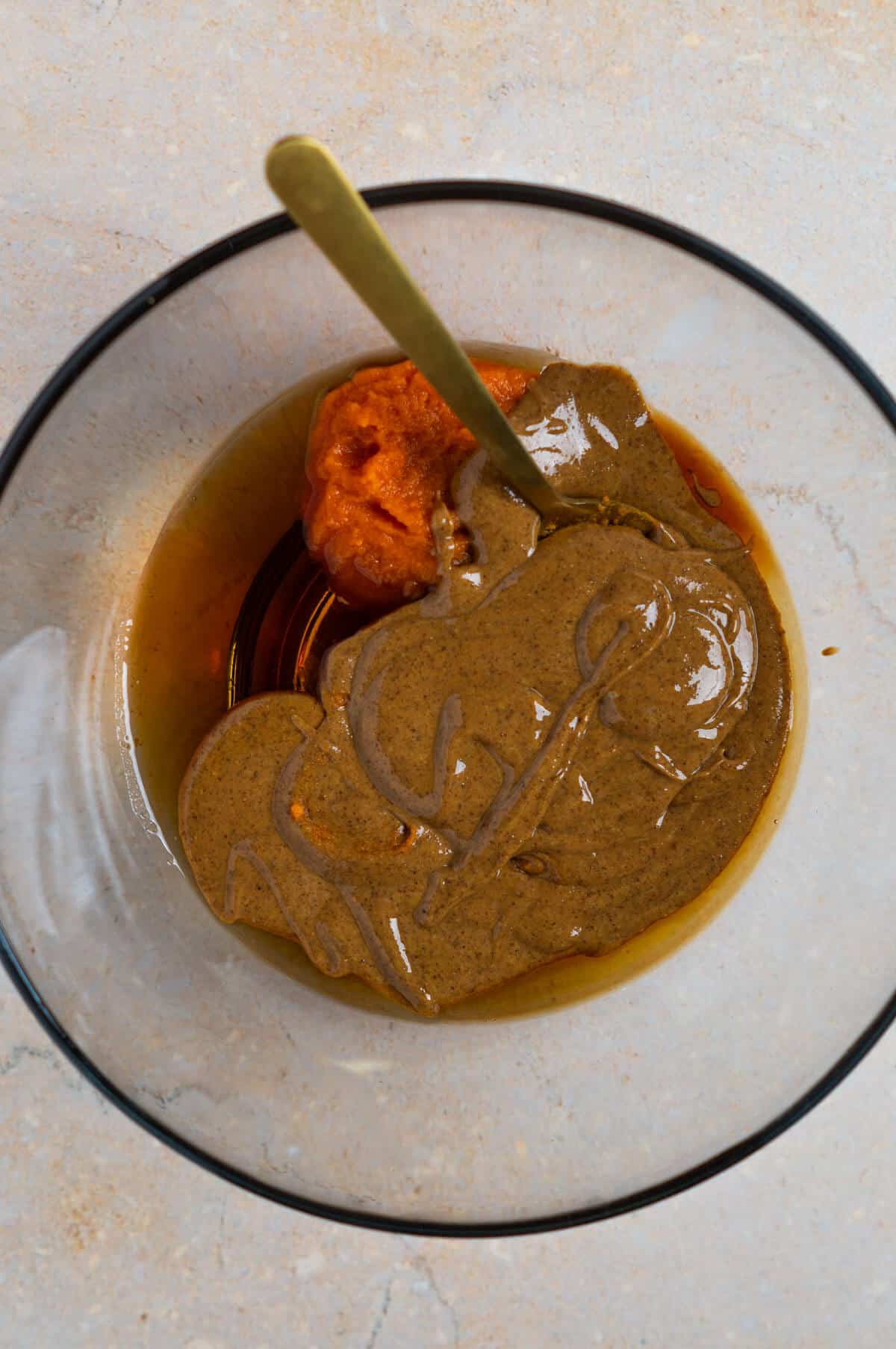 A large mixing bowl with pumpkin puree, almond butter, maple syrup, and vanilla extract.