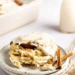 A plate with a brown butter cinnamon roll garnished with two cinnamon sticks.