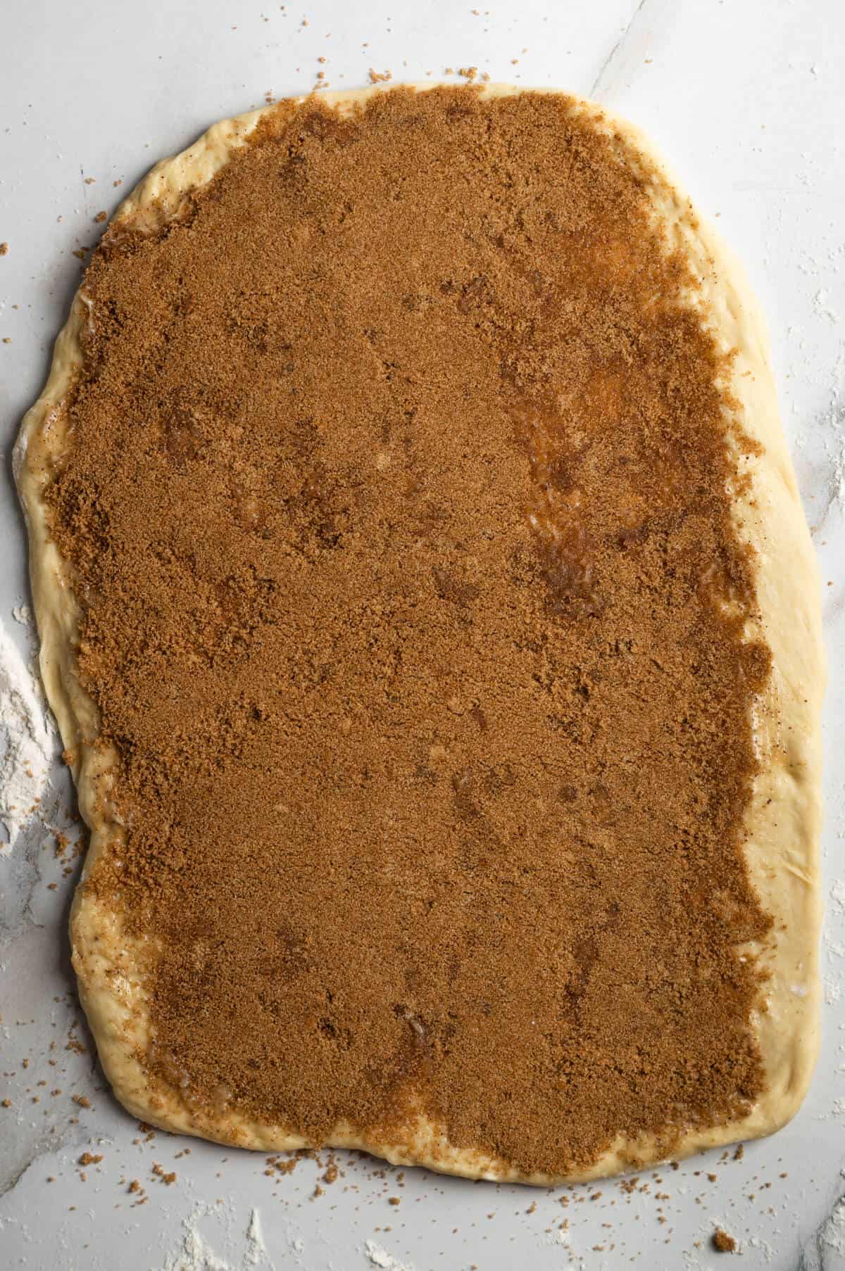 The cinnamon roll dough rolled out into a rectangle with browned butter and the cinnamon sugar mixture spread over the top.