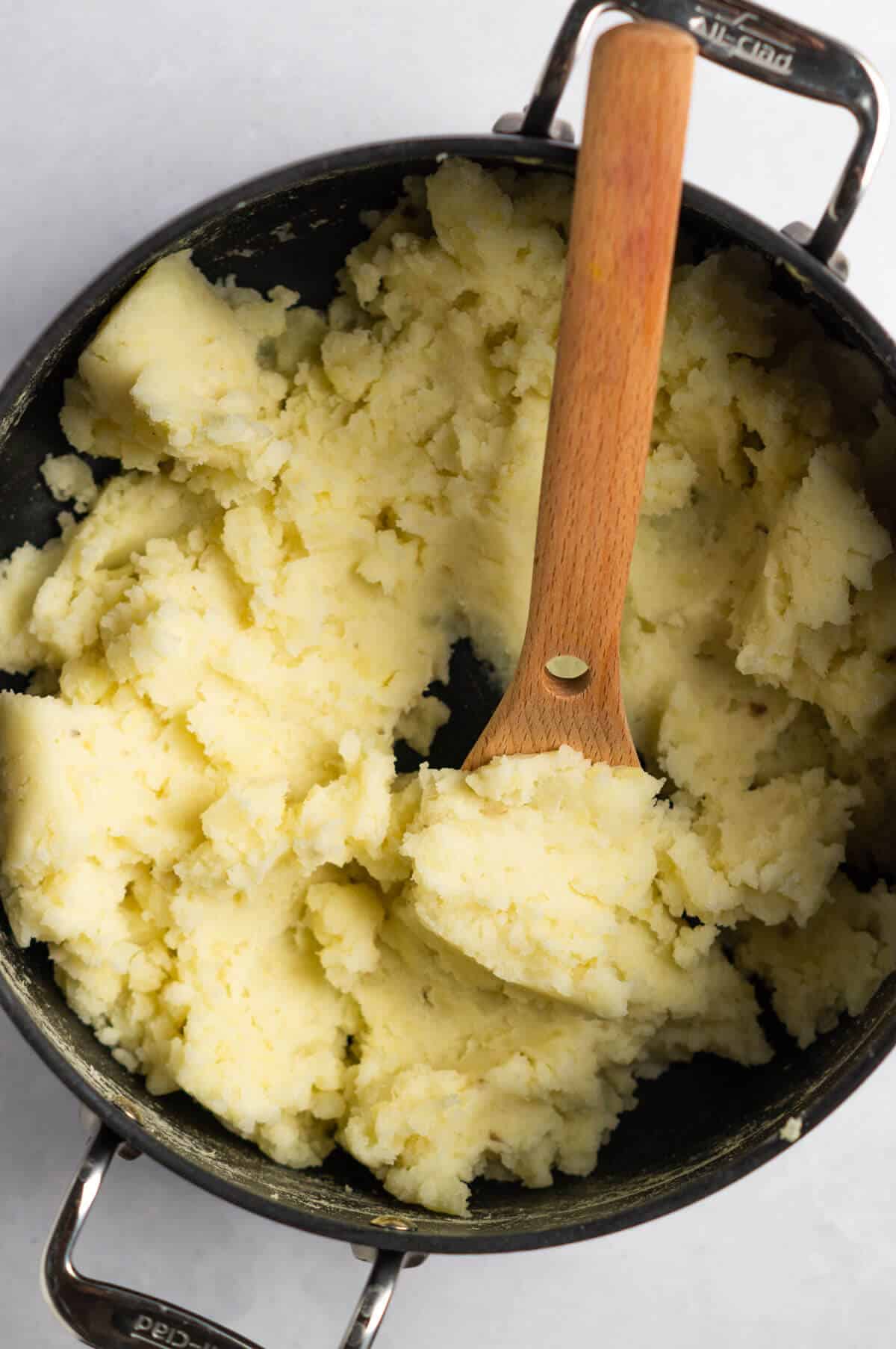 A large pot with mashed potatoes and a wooden spoon.